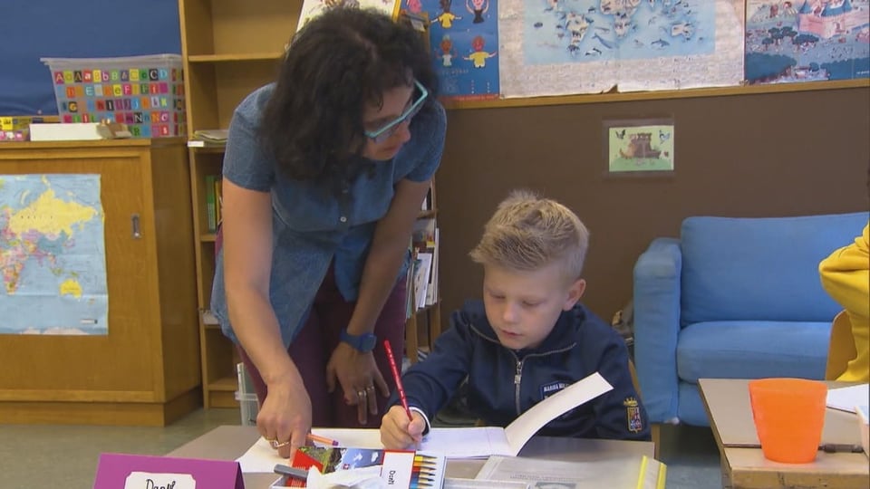 Lehrerin zeigt einem Schüler eine Aufgabe an seinem Pult.