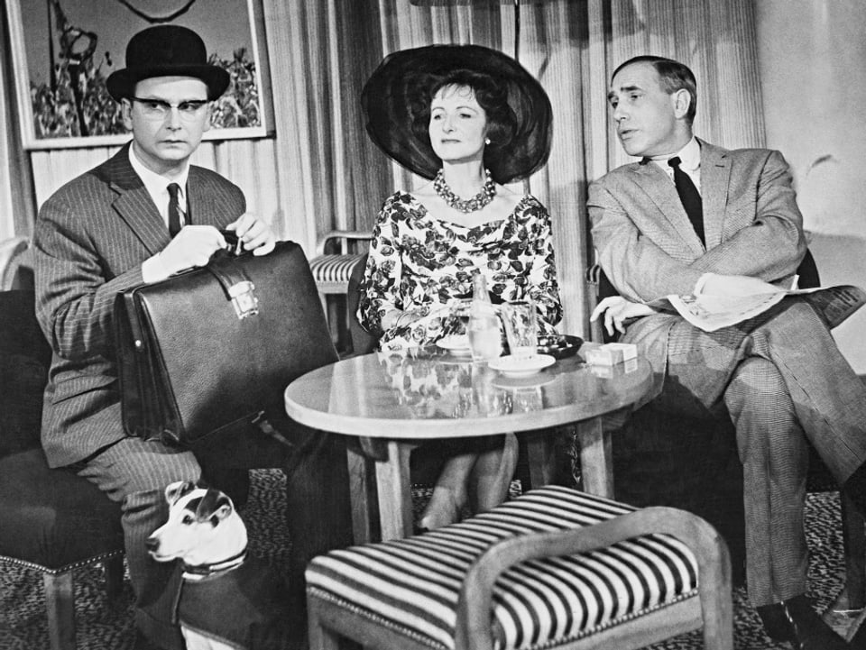 Ein Banker mit einer Aktentasche und einer schwarzen Melone sitzt auf einer Couch. Daneben eine Frau mit Hut und ein Mann mit Anzug.