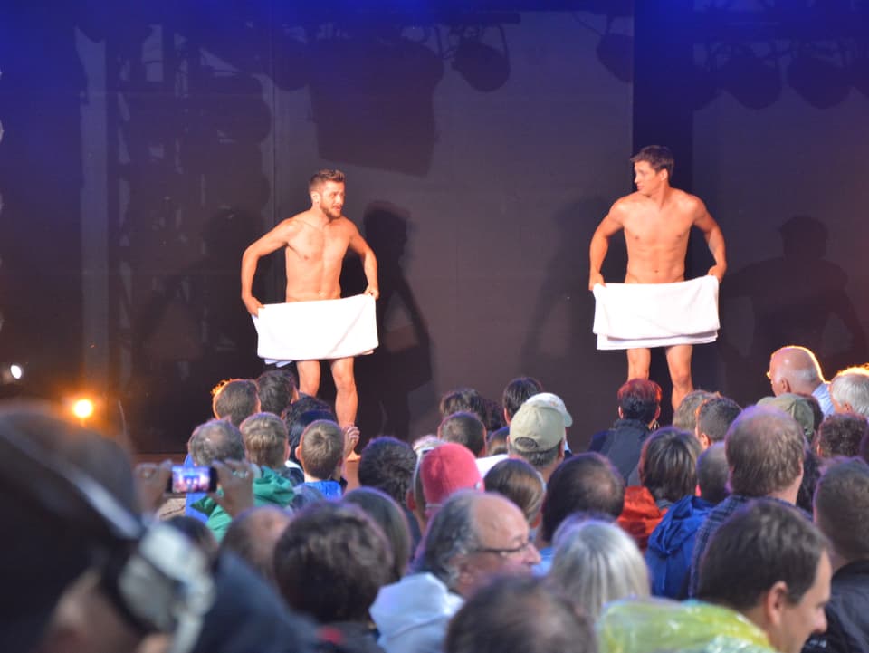 Männer bedecken sich mit einem Badetuch auf der Bühne.