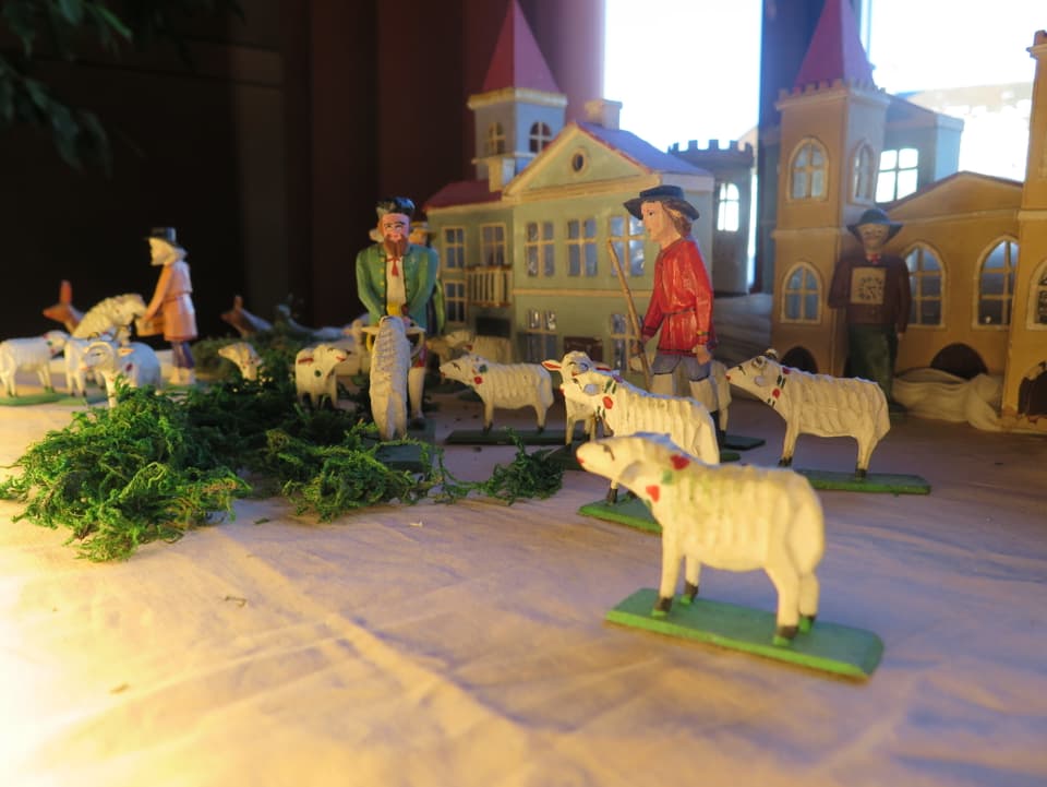 Geschnitzte, weisse Schafe und drei Hirten in rotem, grünem und orangenem Kleid.
