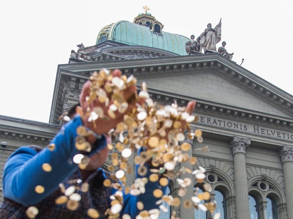 Ein Mann lässt vor dem Bundeshaus in Bern Fünfräppler durch seine Finger rieseln.