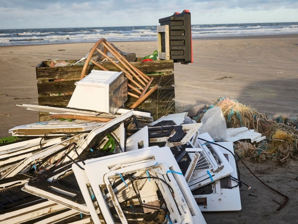 Teile von zerstörten Geräten liegen aufgetürmt auf dem Strand.