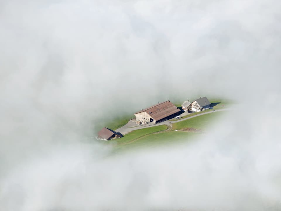 Durch ein Loch im dichten Nebel ist ein Bauernhof zu sehen.