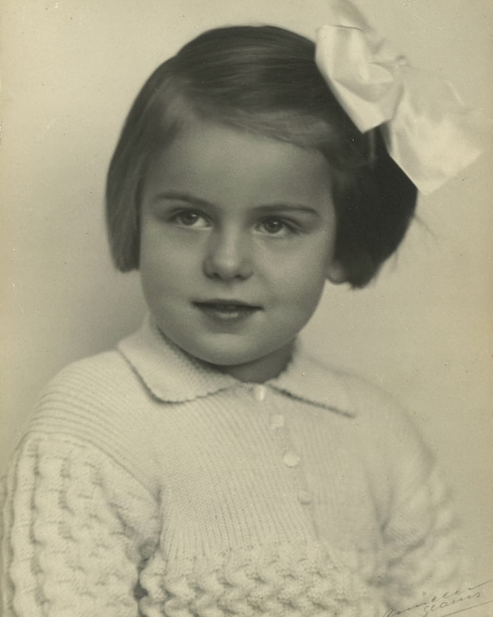 Schwarz-Weiss-Fotografie von einem kleinen Mädchen, das eine grosse weisse Schleife in den Haaren trägt.