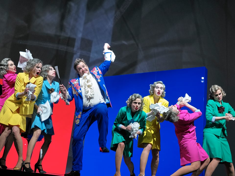Sieben Frauen in pastellfarbenen Kostüm auf einer Theaterbühne.