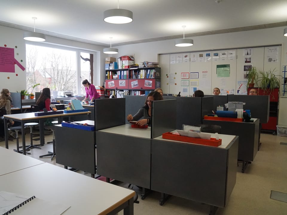 Ein Klassenzimmer ist mit Pulten ausgestattet, die Trennwände haben.