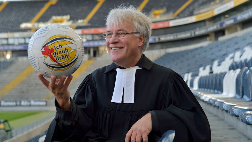 Pfarrer Eckert im Stadion von Eintracht mit einem Ball in der Hand.