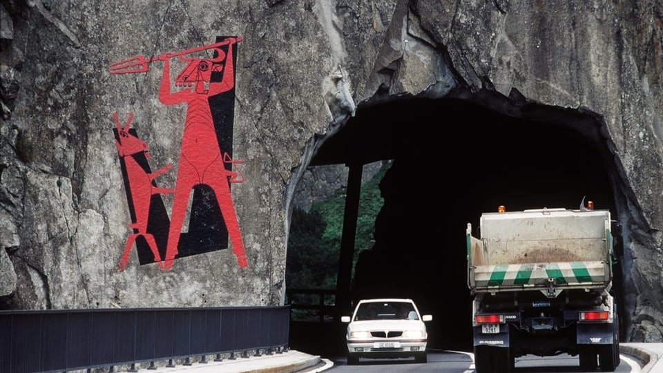 Rotes Bild an Felswand – daneben fahren Autos durch den Tunnel.