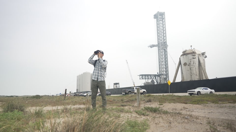 Mann vor STartbasis von SpaceX schaut durch Feldstecher