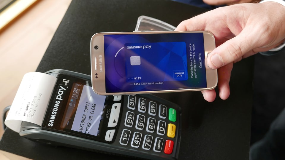 Eine Hand hält ein Smartphone mit Samsung Pay an einen Kreditkartenleser.