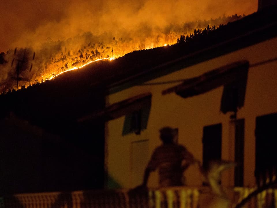 Ein Mann steht auf dem Balkon und schaut den Flammen zu.