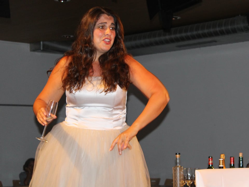 Eine Schauspielerin im weissen Kleid singt auf der Bühne.