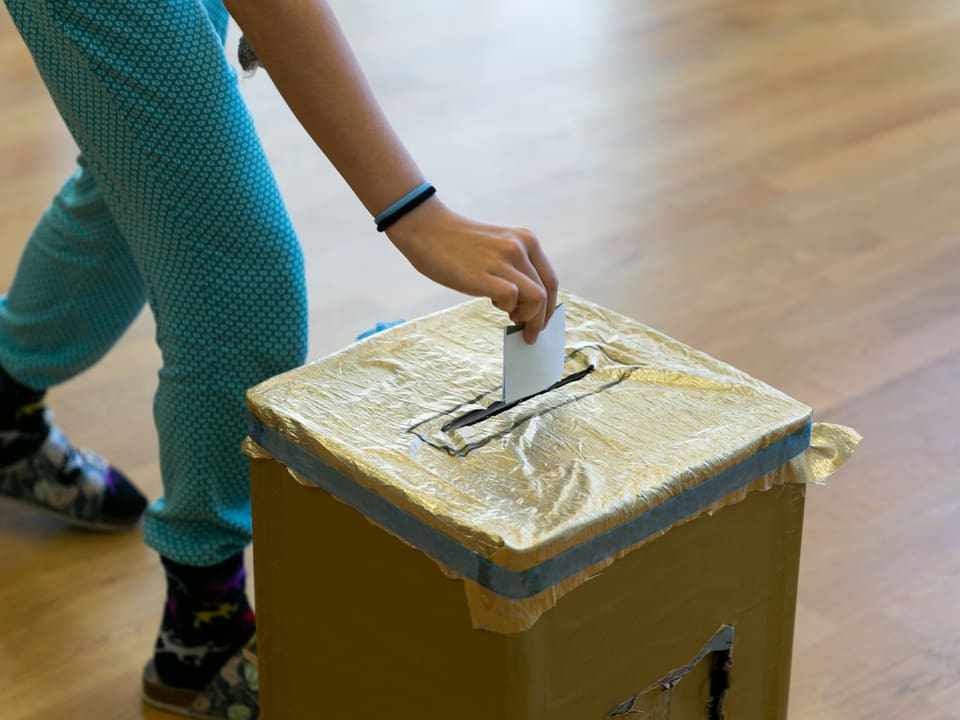 Ein Kind steckt den Stimmzettel in die Wahlurne.