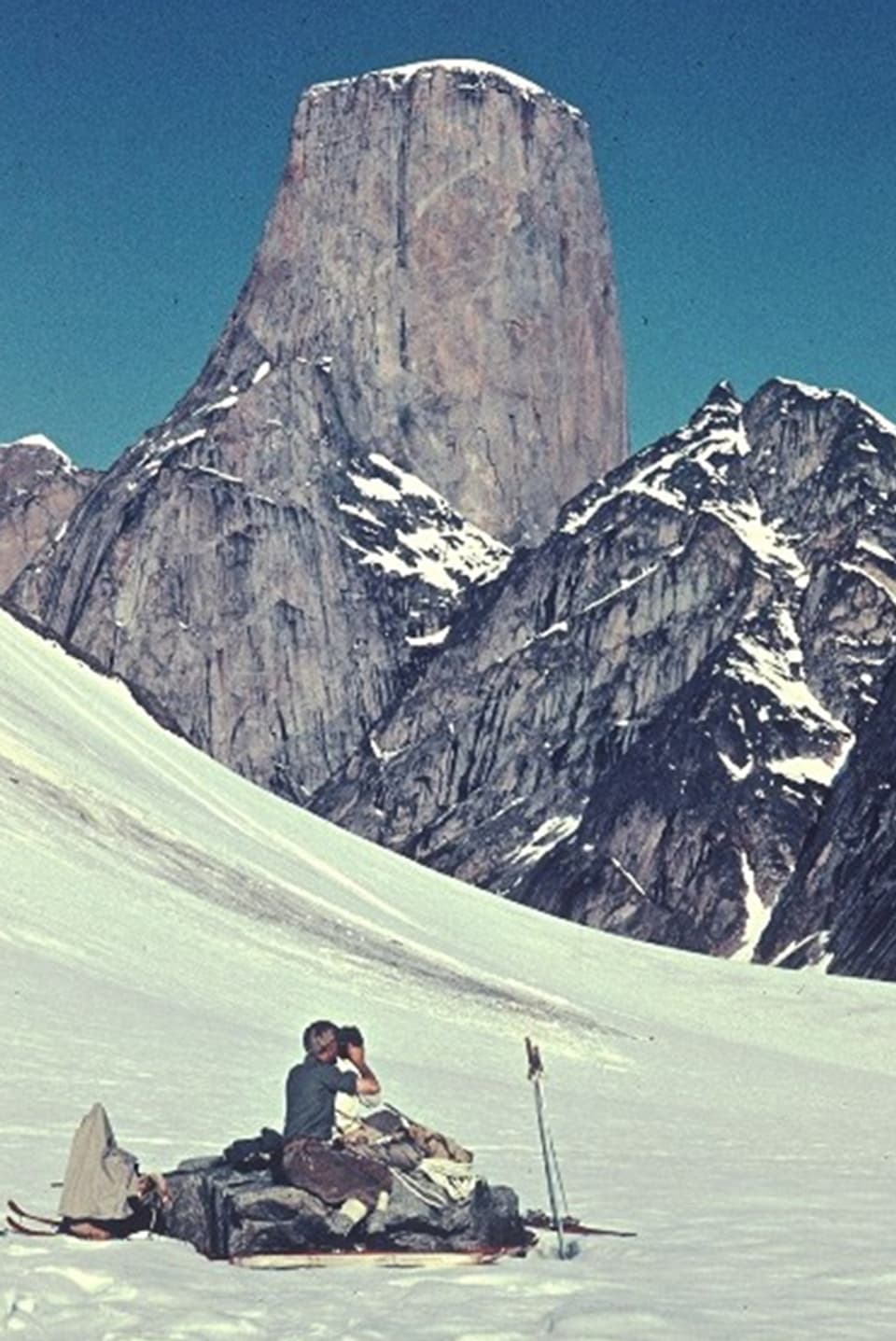 Zwei Expeditionsteilnehmer sitzen mitten auf einem Schneefeld vor einer imposanten Bergkulisse.