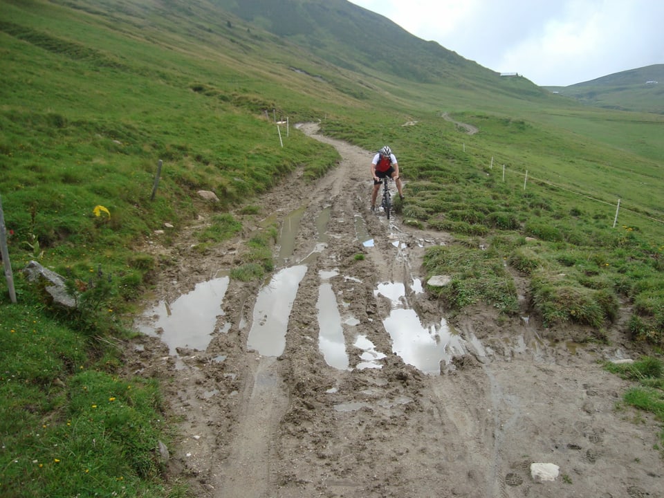 Mountainbiker auf einem Alpweg, der  vom Regen in ein Schlammloch verwandelt wurde.