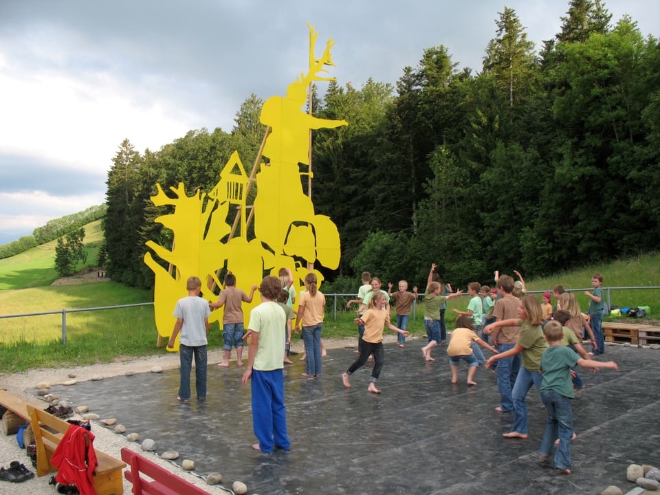 Kinder tanzen barfuss auf einer Bühne, hinter ihnen eine gelbe Skulptur.