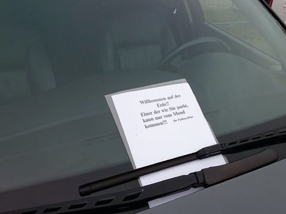 Zettel an der Windschutzscheibe mit dem Text: Willkommen auf der Erde! Einer der wie Sie parkt, kann nur vom Mond kommen.