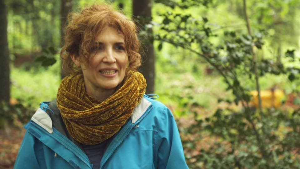 Eine Frau mit Halstuch und Regenjacke im Wald.