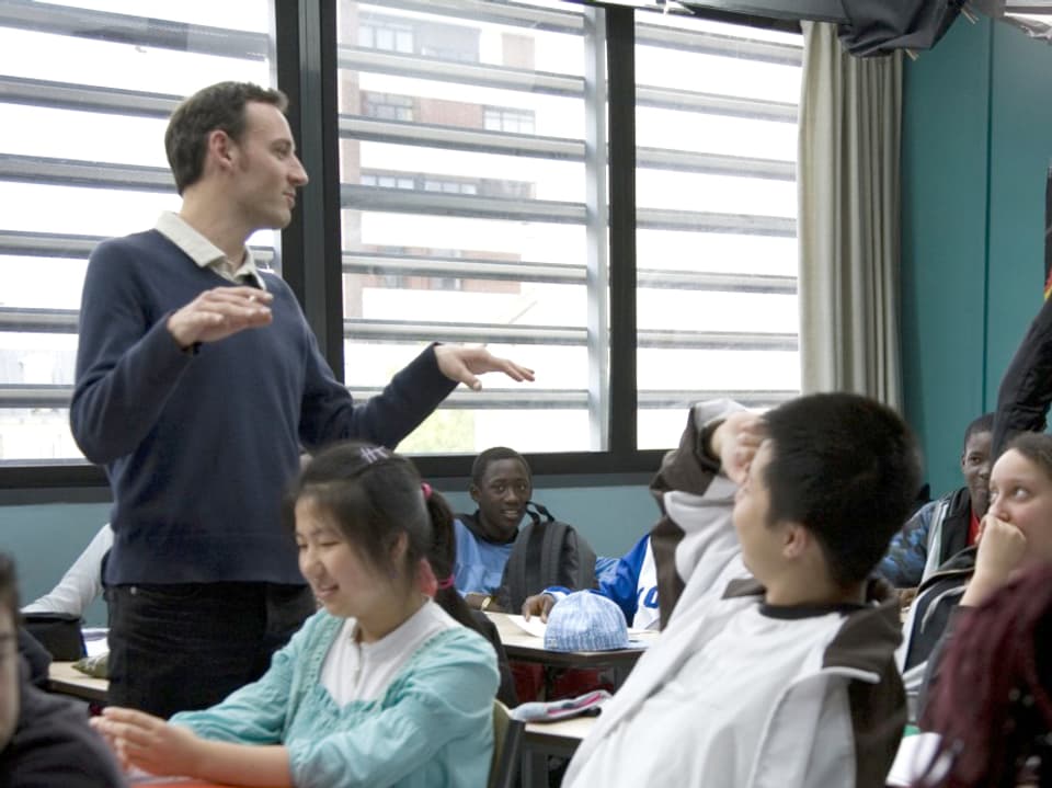 Lehrer François stehend inmitten seiner Klasse, eine Schülerin streckt auf.