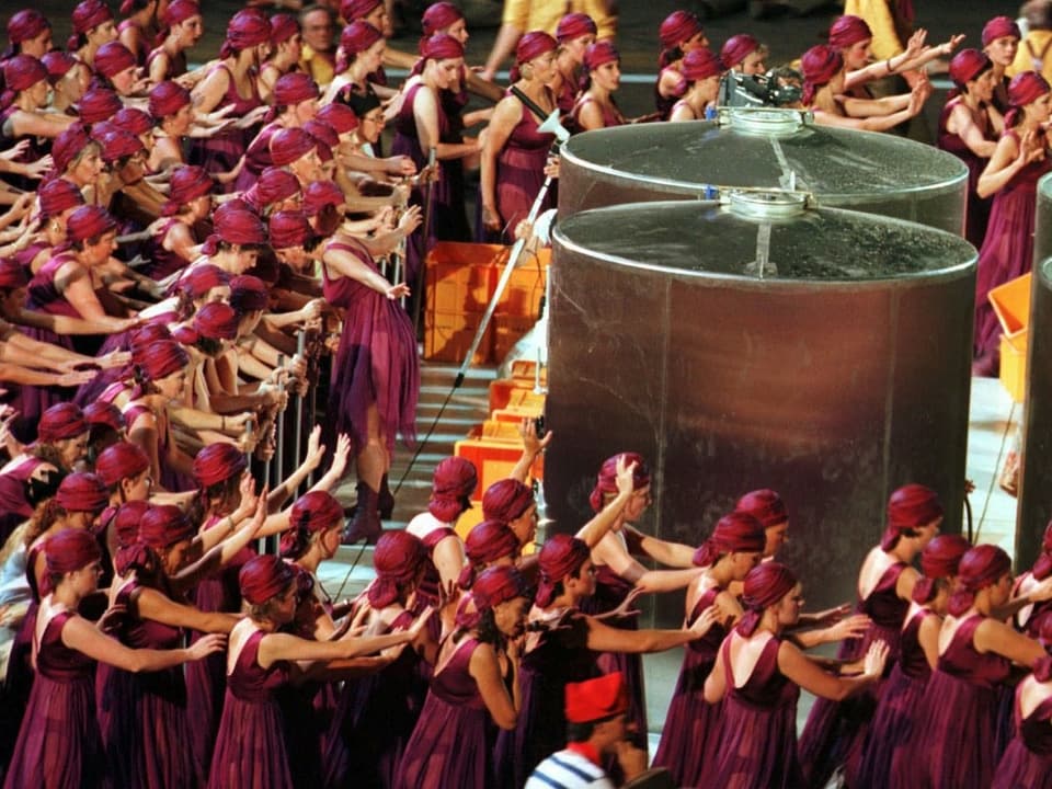Frauen mit Kopftüchern stehen um einen riesigen Weinbehälter.