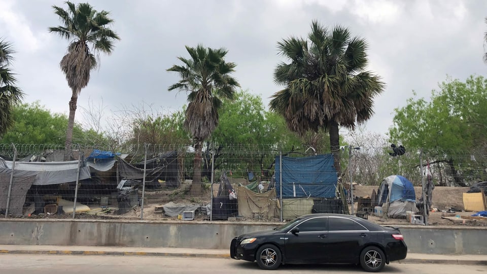 Auto steht vor Zaun hinter dem Reste des aufgelösten Asylcamps in Matamoros.