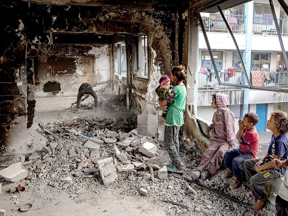 Kinder in zerstörtem Gebäude, Mann repariert Innenraum.