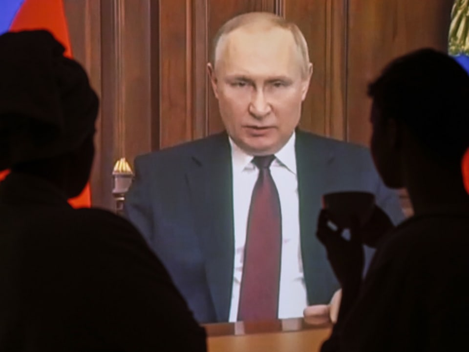 Zwei Personen blicken auf einen TV-Bildschirm, auf dem Wladimir Putin zu sehen ist.