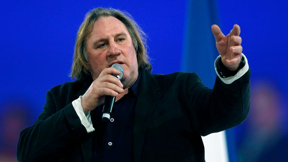 Depardieu mit Mikrofon in der Hand hält eine Rede.
