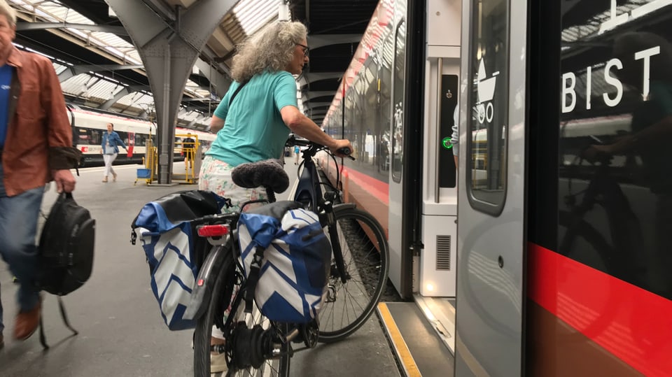 Eine Frau mit einem E-Bike besteigt einen Zug der SOB. 