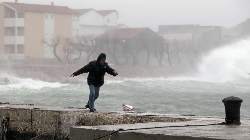 Ein Mann versucht trotz Sturm am Uferweg vorwärts zu kommen.
