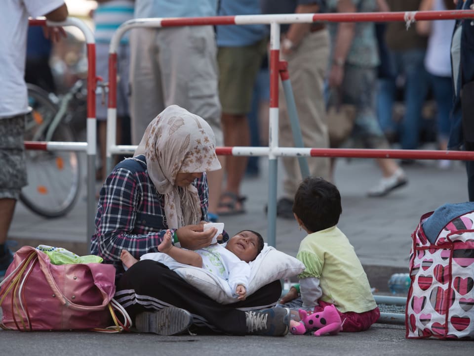 Eine Frau sitzt mit ihren beiden Kindern vor dem Münchner Hauptbahnhof