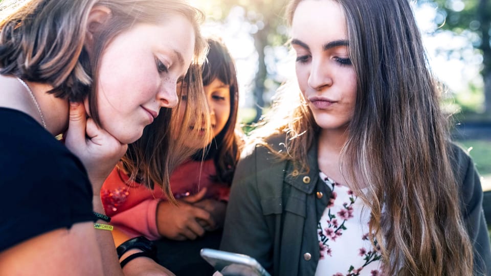 Drei junge Frauen schauen auf ein Smartphone.
