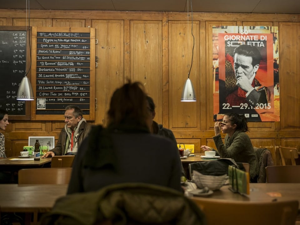 Menschen sitzen in einem Café mit Holzwänden und einem Filmplakat an der Wand.