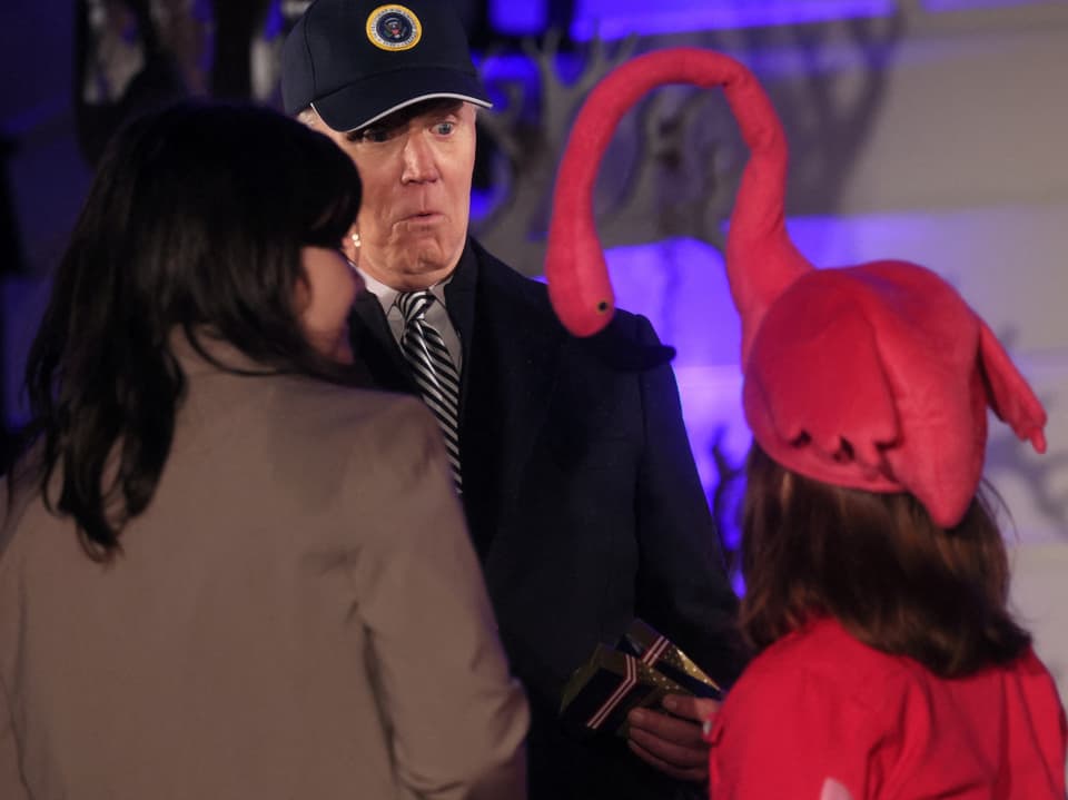 Two people standing in front of the US President wearing Halloween costumes with their backs to the camera.