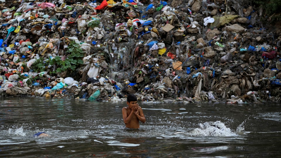 Ein Knabe spielt in einem Fluss, an dessen Ufer sich ein Müllberg auftürmt.