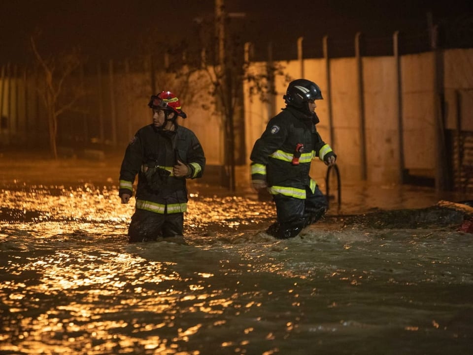 Feuerwehrleute gehen durch die vom Wasser überschwemmten Strassen in der Gemeinde Coltauco. 