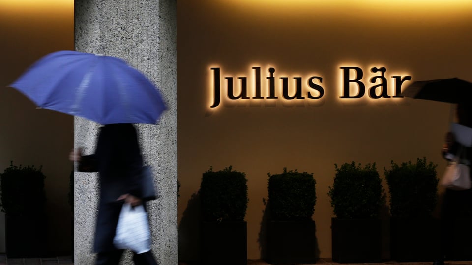 Mann mit Regenschirm vor Julius Bär-Logo 