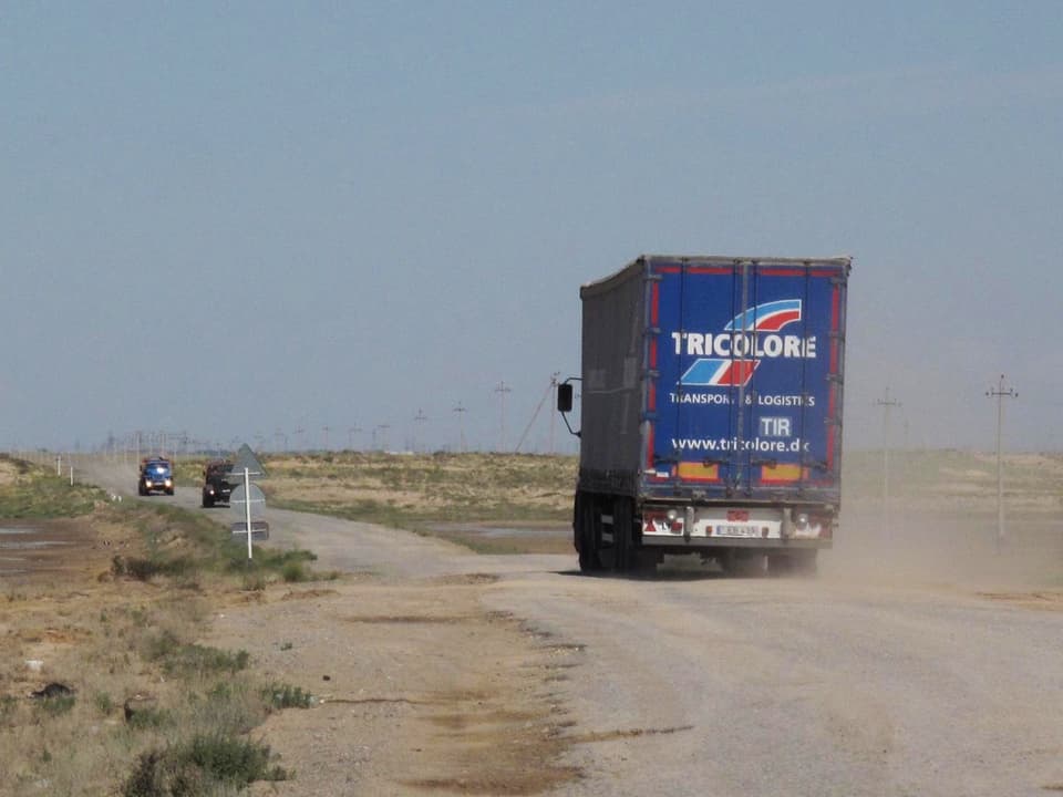 Ein Lastwagen fährt auf einer wenig befestigten Strasse durch die flache Steppe.