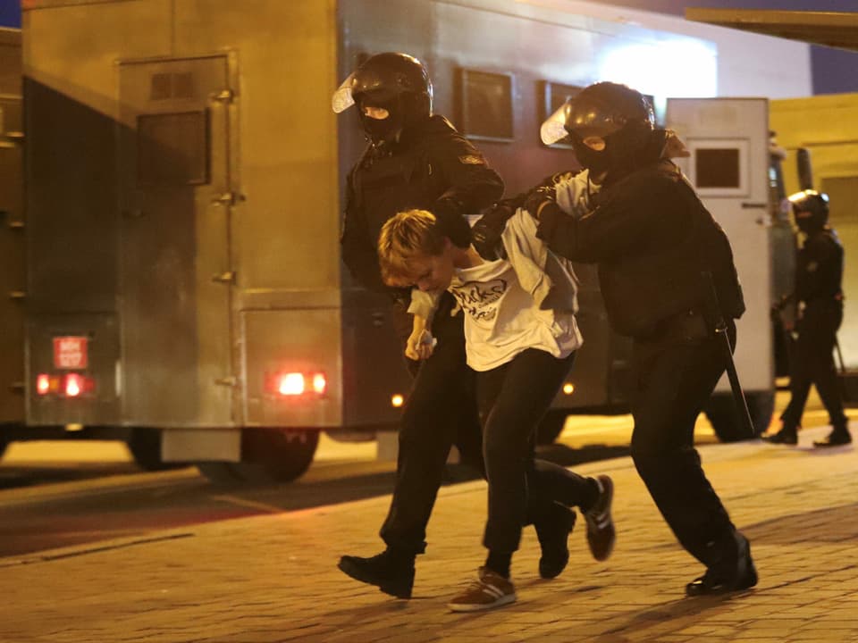 Zwei uniformierte Polizisten führen einen Demonstranten ab.