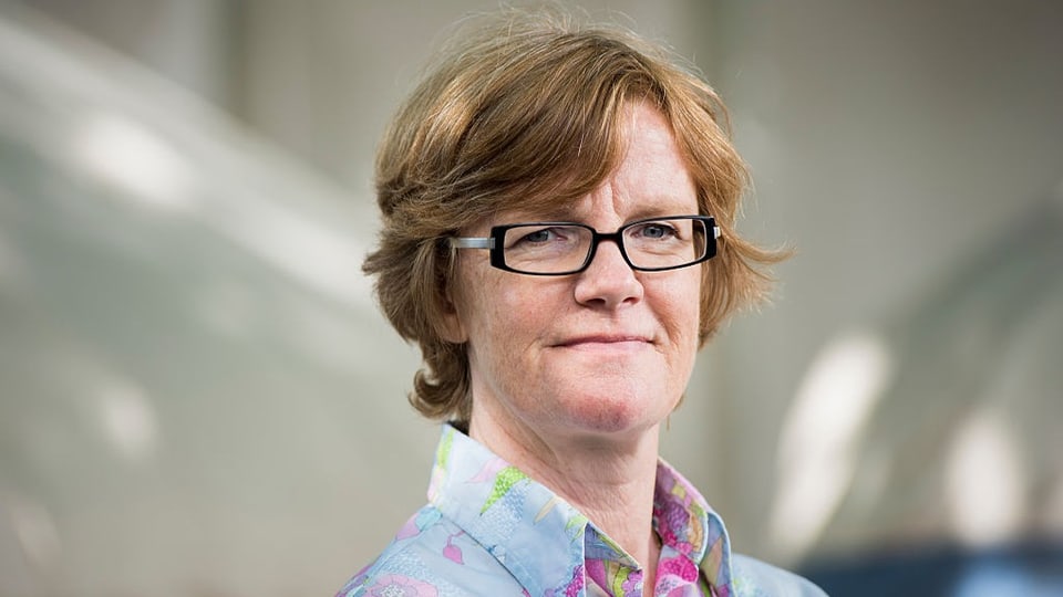 Frau mit Brille und halblangen Haaren blickt in die Kamera.