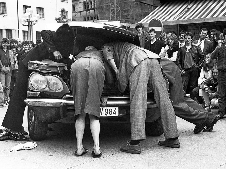 Männer und Frauen beugen sich über einen Kofferraum. 