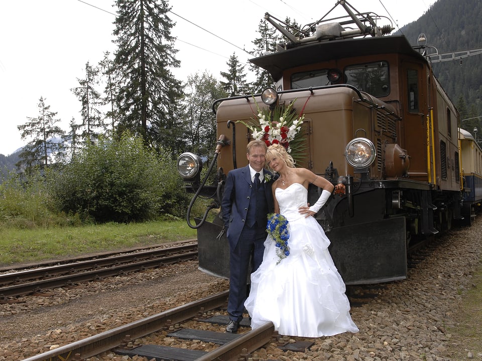 Ein Hochzeitspaar posiert vor einer blumengeschmückten historischen Lokomotive.