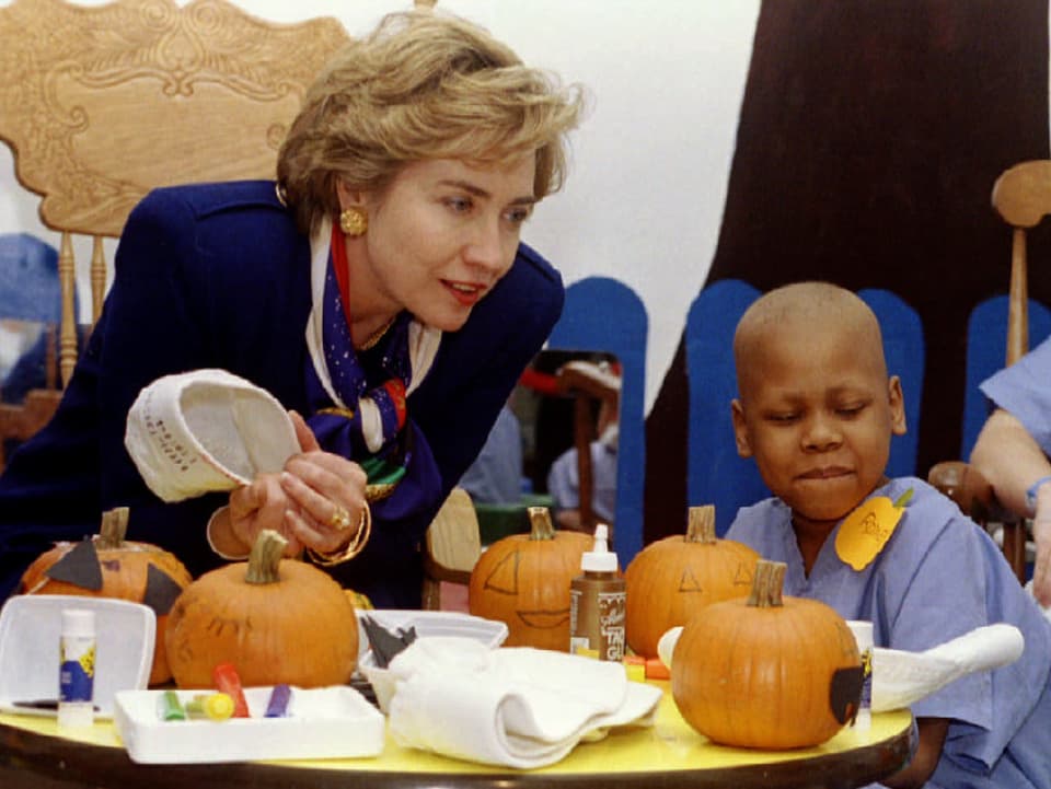 Hillary Clinton sitzt neben einem Kind, das eine Krebsbehandlung erfährt.