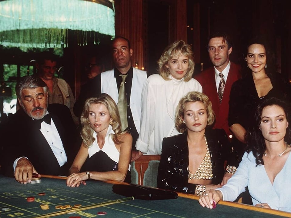 Glamourös angezogene Frauen und Männer sitzen an einem Roulette-Tisch