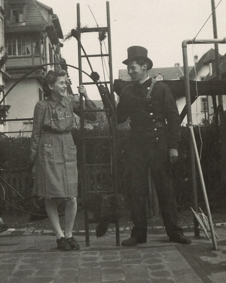 Schwarz-Weiss-Fotografie mit einer Frau und einem Kaminfeger, die sich beide an einer Leiter halten.