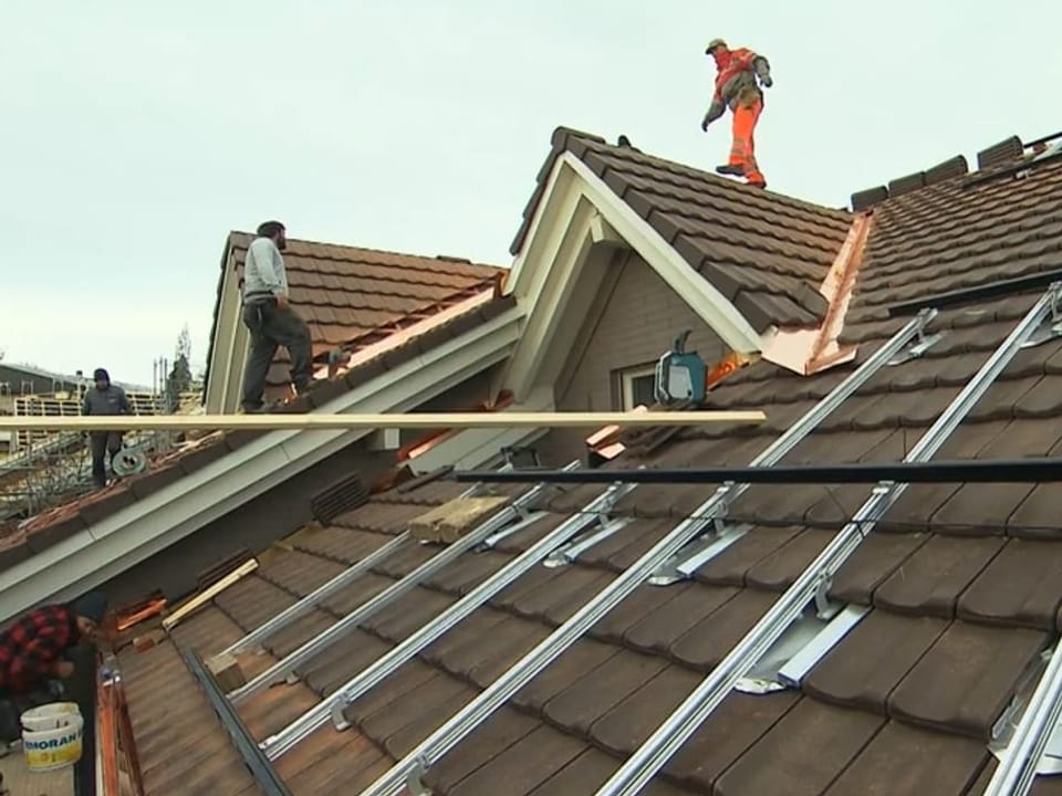 Arbeiter stehen auf einem reparierten Dach. 