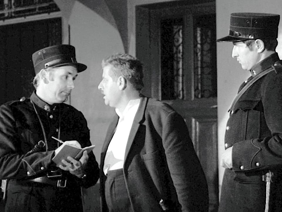 Zwei Polizisten sprechen mit einem Mann, ein Polizist notiert etwas in einem Notizbuch.
