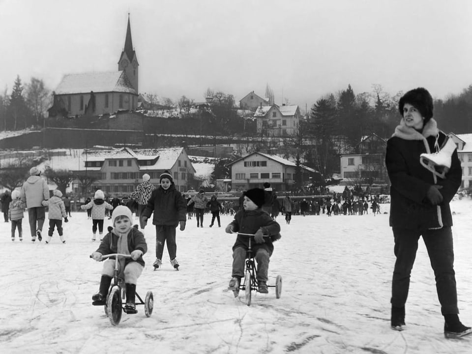 Kinder und Erwachsene vergnügen sich auf Dreirad und Schlittschuhen bei Herrliberg auf dem zugefrorenen Zuerichsee.
