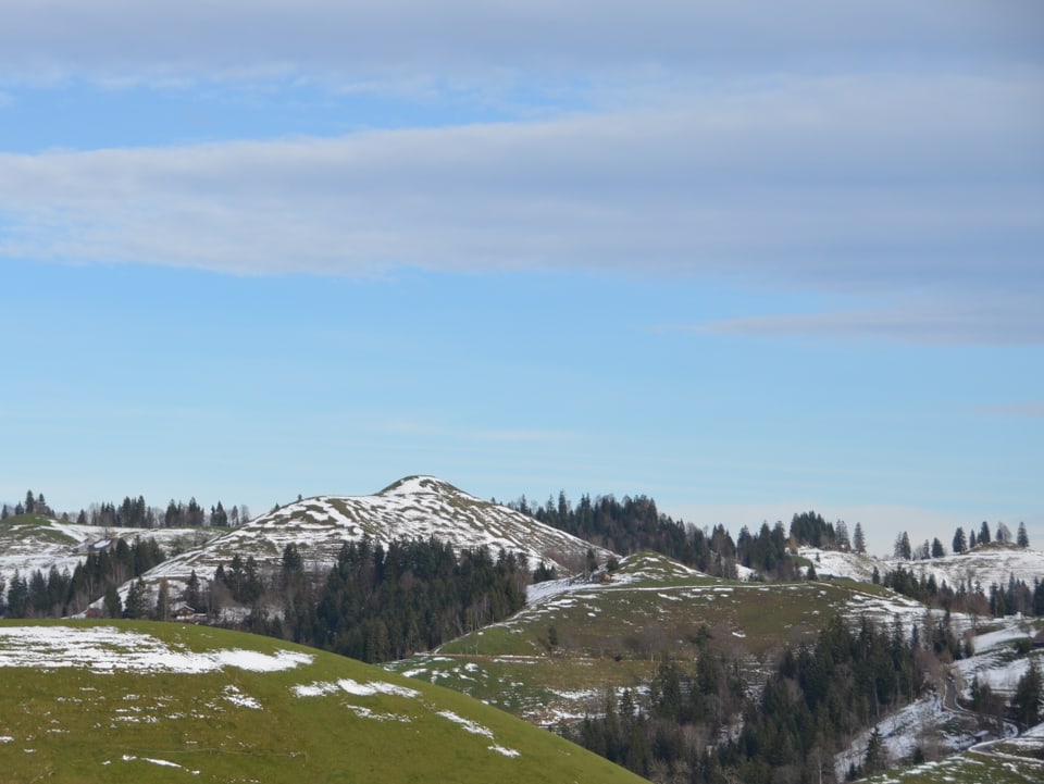 Hügellandschaft mit Schneeflecken auf der Wiese.