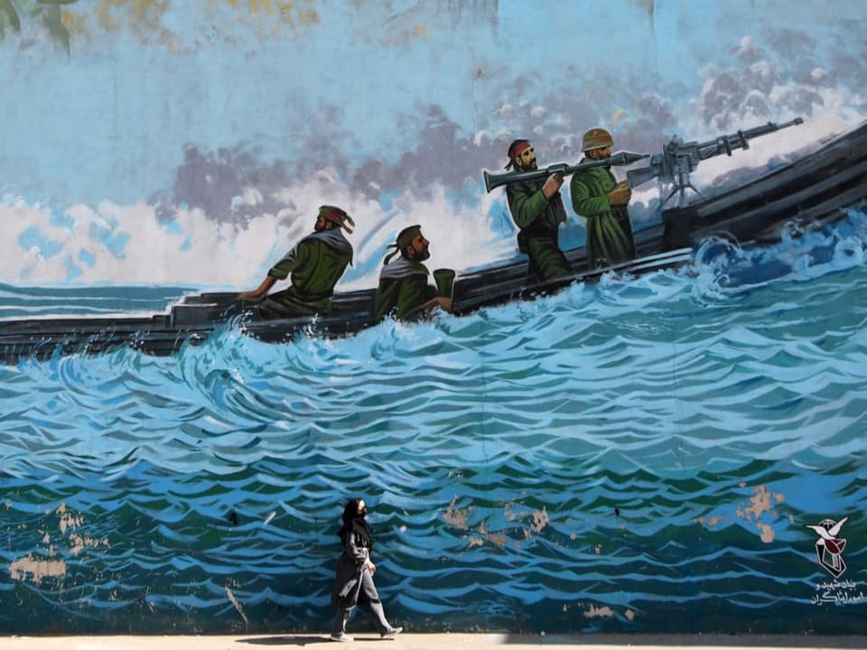 Frau im Kopftuch läuft an einer Wand mit Propaganda-Malerei entlang